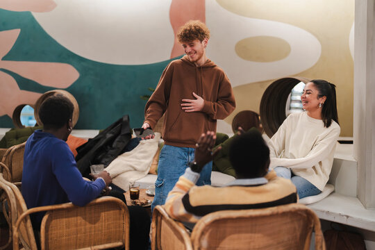 Friends sit together in a cafe with vibrant, artistic wall designs, engaging in a cheerful discussion and sharing a relaxed moment in a modern and sociable environment.