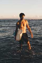 Male athlete with surfboard standing knee deep in sea