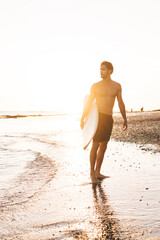 Slim sportsman with surfboard looking at sea on wet shore