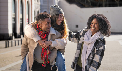 Portrait of happy multi-ethnic friends piggybacking and having fun in the city