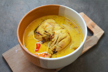 The famous Indonesian chicken curry, served in a bowl on a cutting board. Isolated on gray table.