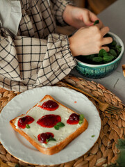 The girl makes a sandwich with jam, decorates with mint leaves. Happy baby makes breakfast. Close-up of children's hands High quality photo