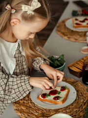 The girl makes a sandwich with jam, decorates with mint leaves. Happy baby makes breakfast