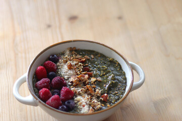 Beige bowl with green smoothie, frozen berries and homemade granola, served on the table. Selective focus.