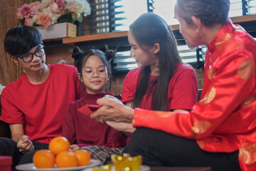 happy asian family gathering at home to celebrate Chinese New Year,sitting on couch,talking,giving red envelope and eating