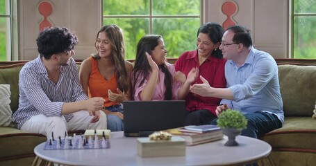 Indian happy young adult multi family group mom dad sitting cozy sofa couch use laptop watch movie film give high five teen girl child male female man boy look show enjoy have fun joy spend day time - Powered by Adobe