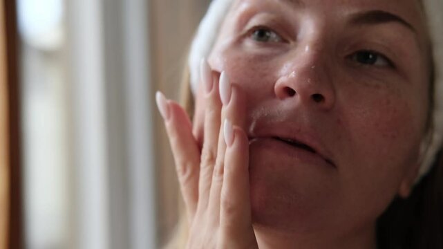 a woman gives herself a face and neck lifting massage with anti-aging serum or essentials oil, facial skin care