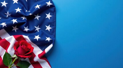 Obraz premium A single red rose rests gently upon a folded American flag against a vibrant blue backdrop, creating a poignant and symbolic composition.