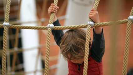 Cute baby toddler holding into playground rope. Child exercise outdoors