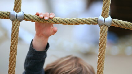 Cute baby toddler holding into playground rope. Child exercise outdoors