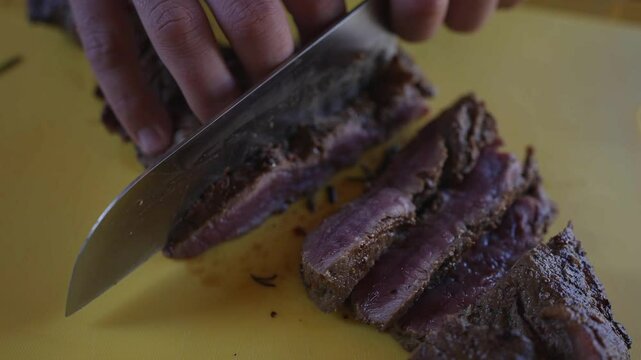 A person is cutting a piece of meat with a knife. The meat is cut into three pieces