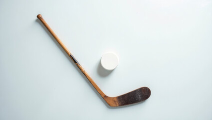 A vintage hockey stick lies next to a puck on a clean white background. The image evokes nostalgia and a sense of history