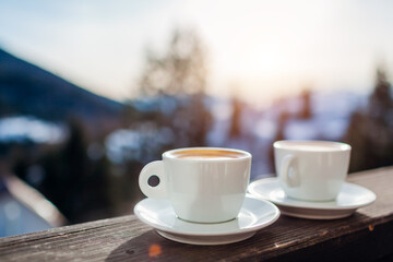 Close up of coffee for two in winter mountains during holidays. Couple of white cups with hot drinks on hotel balcony.