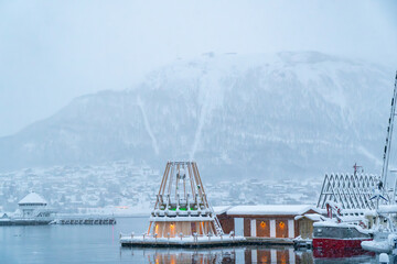 Tromsø, Norway, city harbor with a sauna and bath, mainland and mountains in the background. Polar night, snowstorm