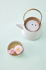 Colorful daisies floating in a delicate bowl beside a vintage teapot on a soft green surface