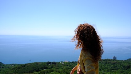 Obraz premium A young woman stands on a mountain peak with arms outstretched, admiring the vast ocean below. The scene captures a sense of freedom, serenity, and connection to nature.