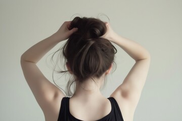 Obraz premium Rear view of a young woman gathering her long brown hair in a messy bun against a white background