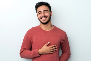 Portrait of a cheerful young man holding his hand on his chest, showing heartfelt emotion and appreciation, against a white background