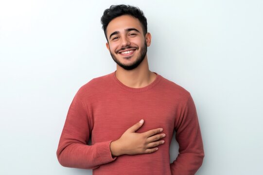 Portrait of a cheerful young man holding his hand on his chest, showing heartfelt emotion and appreciation, against a white background