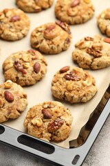 Tasty cookies with nuts in baking tray on gray textured table, closeup