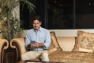 Fototapeta premium Happy latin man chatting on phone with friends in modern cozy space