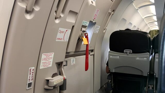 This captures a close-up of the emergency exit door inside an airplane cabin, highlighting safety instructions and seating arrangements while passengers await takeoff.