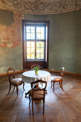 A round table and three chairs in the rooms of an ancient medieval castle, light from the window