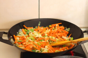 Sauteing chopped leek and carrot slices in a wok. Selective focus.