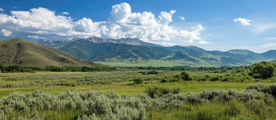 Obraz premium Vast green landscape with mountains and clouds under blue sky featuring Copy Space for text insertion