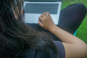 Bokeh. A student girl is typing a college assignment using a laptop in the yard in the afternoon. Photographed with a blurry background