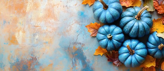 Autumn landscape with vibrant blue pumpkins surrounded by orange and brown leaves on a textured blue background ideal for seasonal promotions.