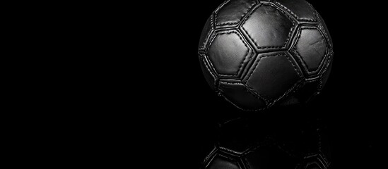 Black leather soccer ball positioned on a dark reflective surface, creating a striking contrast and ample space for text insertion.