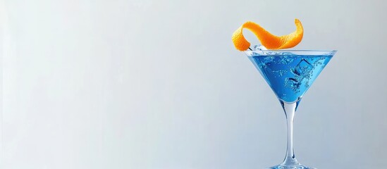 Blue martini cocktail with orange peel garnish in a clear glass, close-up on a light gray background, featuring vibrant blue and bright orange colors.