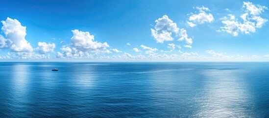 Aerial view of bright blue ocean horizon with a solitary yacht on calm waters under white clouds and ample copy space for text