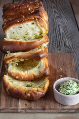 Homemade fresh pull apart bread with herbs (parsley, thyme, rosemary, dill), garlic, cheese and spicy butter on a wooden board.