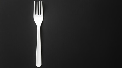 White plastic fork on a black background with ample copy space for text placement. Simple and minimalistic design for food-related use.