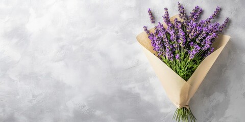 Fresh bouquet of lavender flowers wrapped in brown paper on textured gray background with copy space for branding or text.