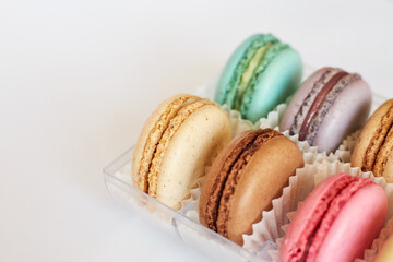 French Macarons with white paperpan in plastic transparent packaging box on gray background, colorful cakes with various flavors. appetizing dessert, macaroons. Copy space for text, top view