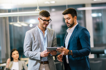Two colleagues talking in corridor. Using tablet for the job.