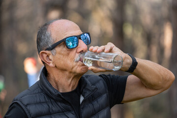 A man is peacefully drinking water while having a tranquil moment deep within the lush woods around him. Portrait, Horizontal