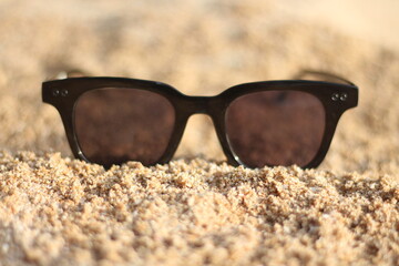 A black sunglass placed on the beach on holiday. Stylist black sunglasses on sand.