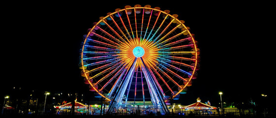 Colorful ferris wheel light trails creating a vibrant night display against a black background
