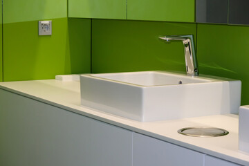
A white, square basin with a chrome mixer, mounted on a white worktop in a bathroom with a bright...