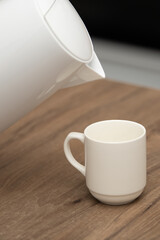 Hot drip coffee being poured into a white cup on a wooden table in a cozy kitchen setting