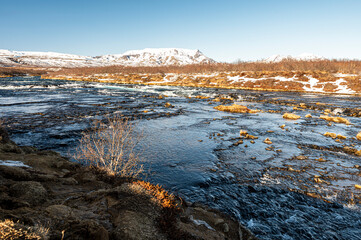 View over the river from the buarfoss waterfall. The water is frozen and the ground is covered in snow