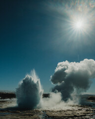 Strokkur geysir erupting under bright sunlight, releasing steam and water in south Iceland