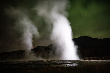 Nighttime view of Strokkur geysir erupting under the northern lights in south Iceland