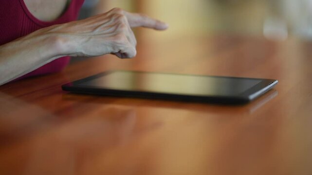 Hand pointing at a tablet screen with a gren reflection on a wooden table