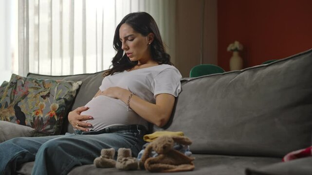 Young woman sitting on a cozy couch, experiencing the early stages of labor contractions, capturing the anticipation, excitement, and emotional journey of approaching childbirth
