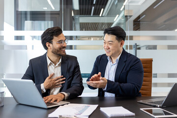 Two colleagues at workplace, Senior boss praising subordinate for excellent results achievement at workplace. Men working together inside office at workplace with laptops.